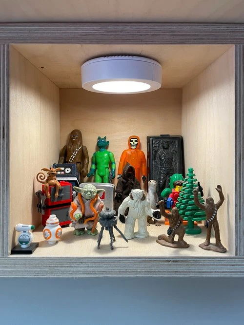 Aaron Draplin's plywood shelf displaying Star Wars and pop culture collectible figures under a puck light