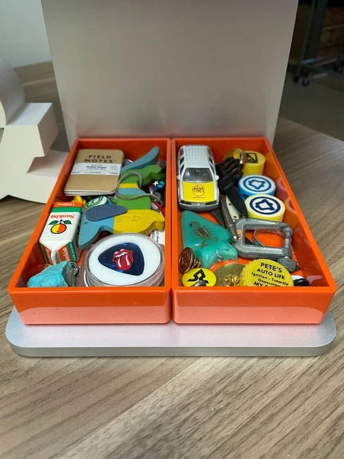 Aaron Draplin's two orange desk organizer trays filled with colorful pins, keychains, a toy car, and collectibles