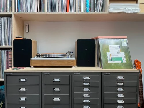 Aaron Draplin's Shinola turntable with speakers atop Bisley flat file drawers, surrounded by his extensive vinyl record collection