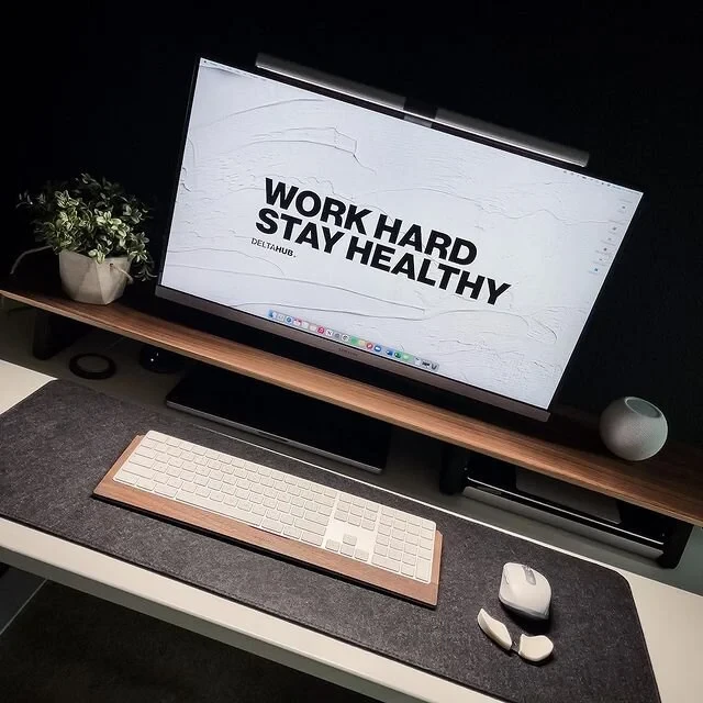 LizzLovesTech's desk with a 'Work Hard Stay Healthy' monitor wallpaper, BenQ ScreenBar, Magic Keyboard on a wooden tray, and Apple mouse