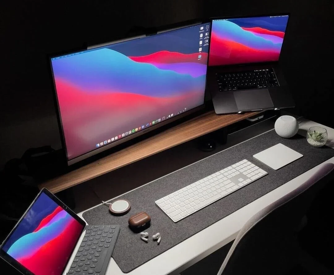 LizzLovesTech's Apple desk setup with dual monitors, Magic Keyboard, AirPods, and iPad on a dark felt desk mat