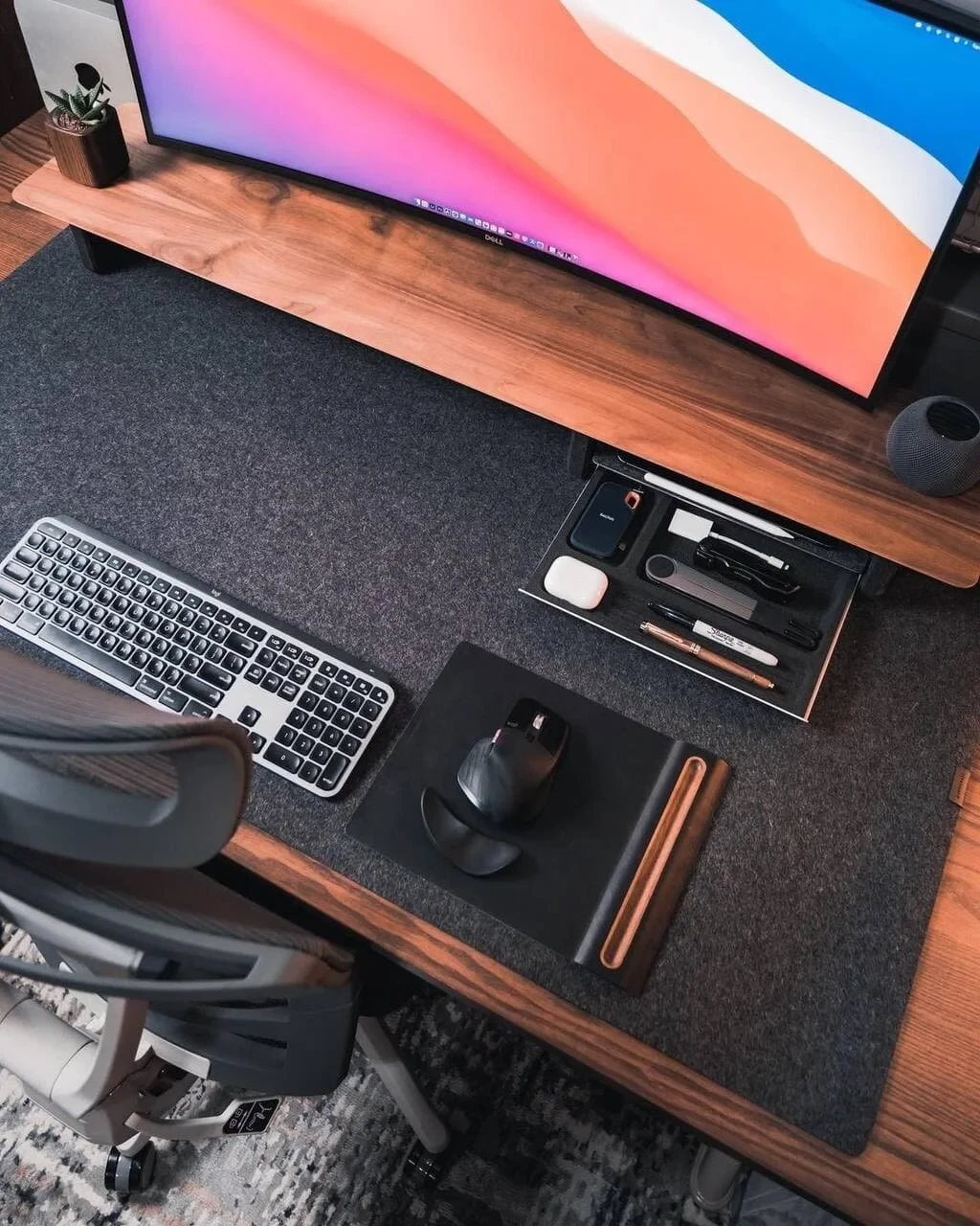 Overhead view of Lloyd Carig's walnut desk with curved ultrawide monitor, Apple Magic Keyboard, and dark felt desk mat